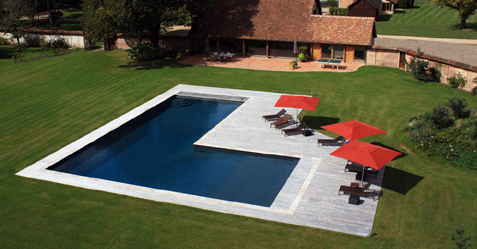 Piscine extérieure en forme de L au milieu d'une pelouse fraichement coupée